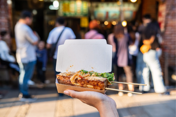 Main tenant une boîte de nourriture de rue avec brochettes