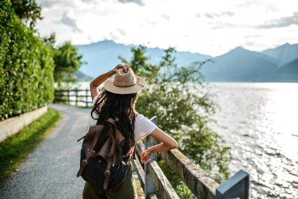 Femme avec sac à dos et chapeau regardant un lac et des montagnes