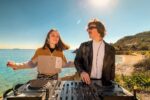 Amii Watson et Jimmi Harvey, duo de DJs derrière la chaîne YouTube Flavour Trip, mixant de la house music sur une plage ensoleillée.