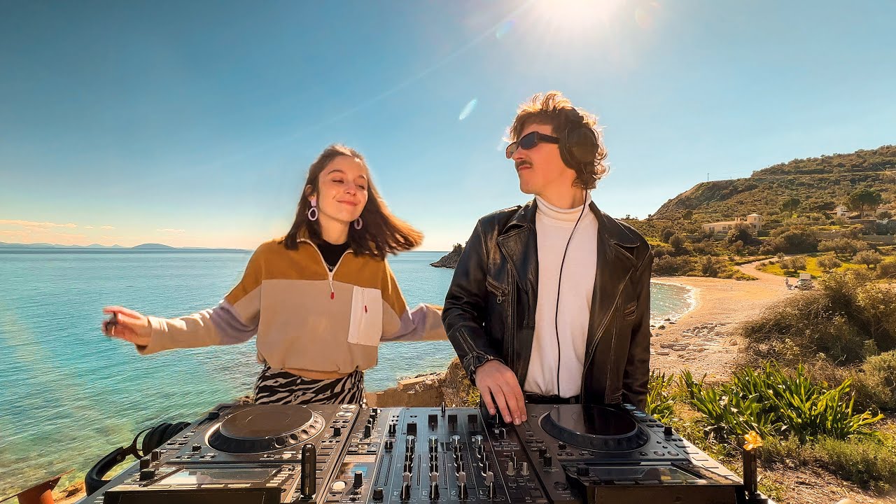 Amii Watson et Jimmi Harvey, duo de DJs derrière la chaîne YouTube Flavour Trip, mixant de la house music sur une plage ensoleillée.