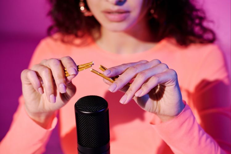 Femme pratiquant l'ASMR avec des bâtons en bois devant un microphone pour créer des sons relaxants.