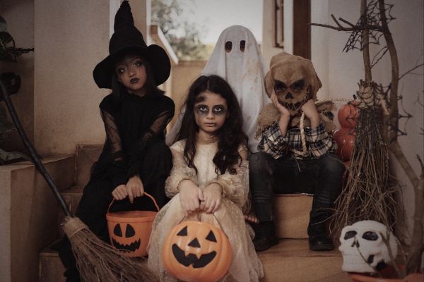 Enfants déguisés en sorcière, fantôme, squelette, et zombie assis sur des marches, prêts pour Halloween.