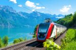 Train rouge et blanc circulant le long d'un lac et des montagnes, représentant un voyage en train éco-responsable en Europe.