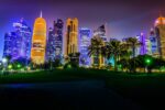 Skyline de Doha la nuit avec des bâtiments modernes illuminés et des palmiers.