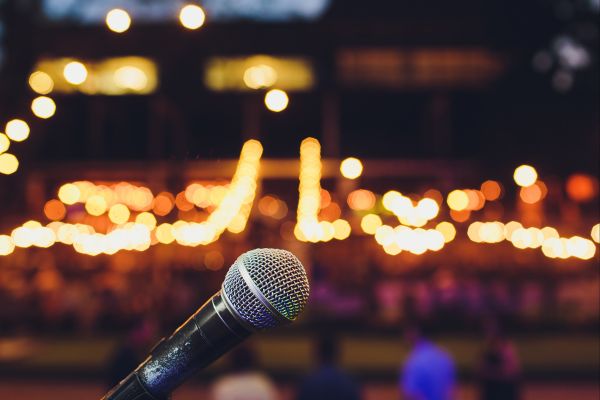 Microphone sur scène de stand-up français, humoristes français, avec un public en arrière-plan, ambiance lumineuse et festive.