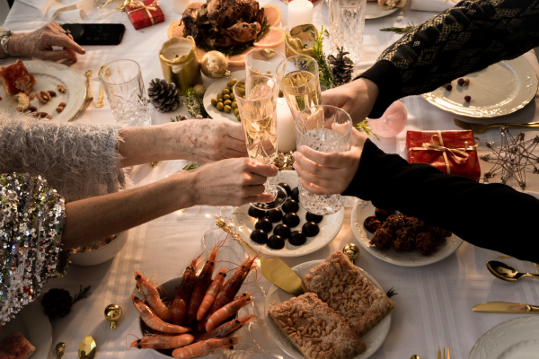 Photo d'un repas de Noël en famille, avec des mains portant des verres pour trinquer, une table décorée de fruits de mer, de bougies et de cadeaux. Crédit photo : Sheena Diolle - Studio Spain.