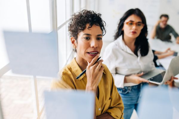 Deux femmes réfléchissant à une stratégie marketing en analysant des notes sur un tableau, illustrant le concept du marketing émotionnel